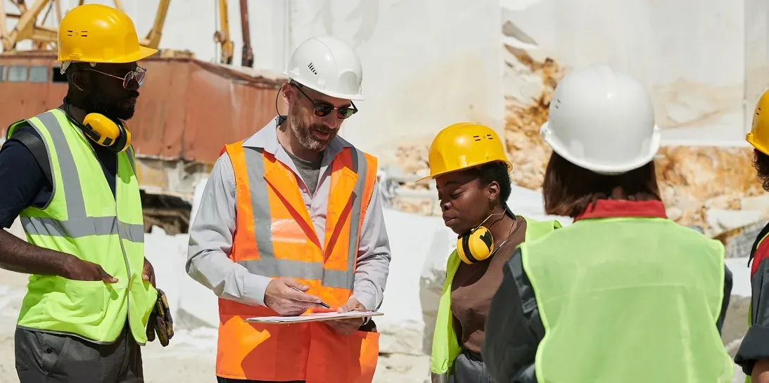 Confident foreman in uniform and safety helmet pointing at document with plan